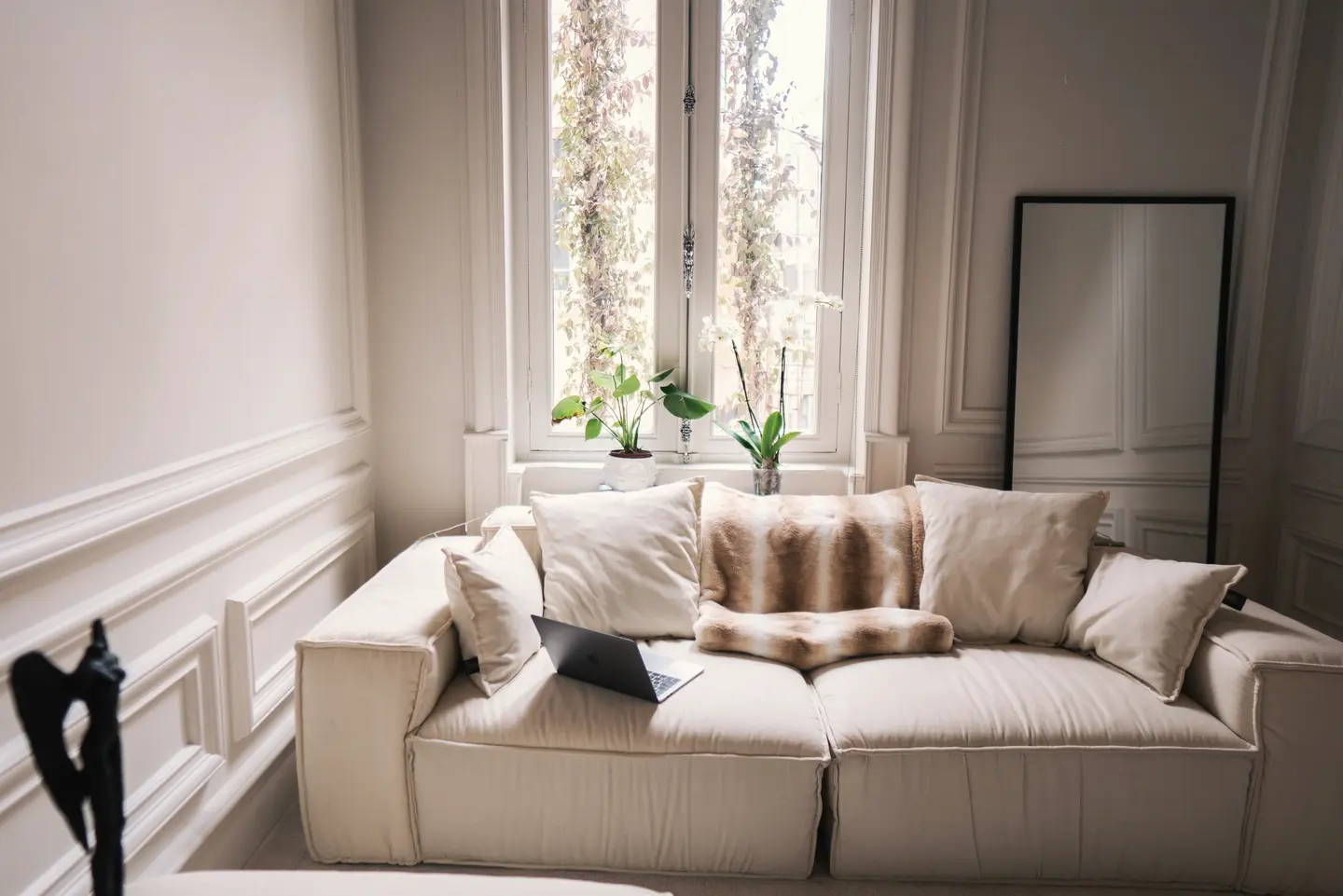 Sala clara com sofá modular off-white de dois módulos diante de uma janela alta com plantas