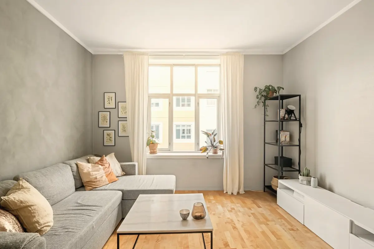 Sala de estar com sofá cinza com chaise, mesa de centro e janela com cortinas claras